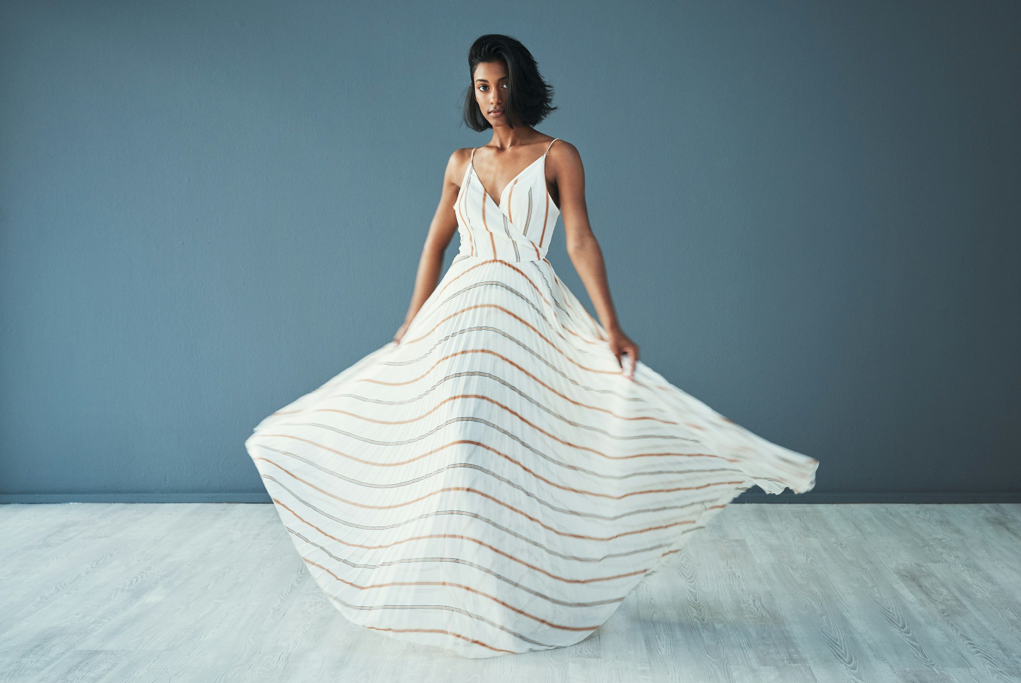 Shot of a beautiful young woman wearing a long flared dress against a blue background