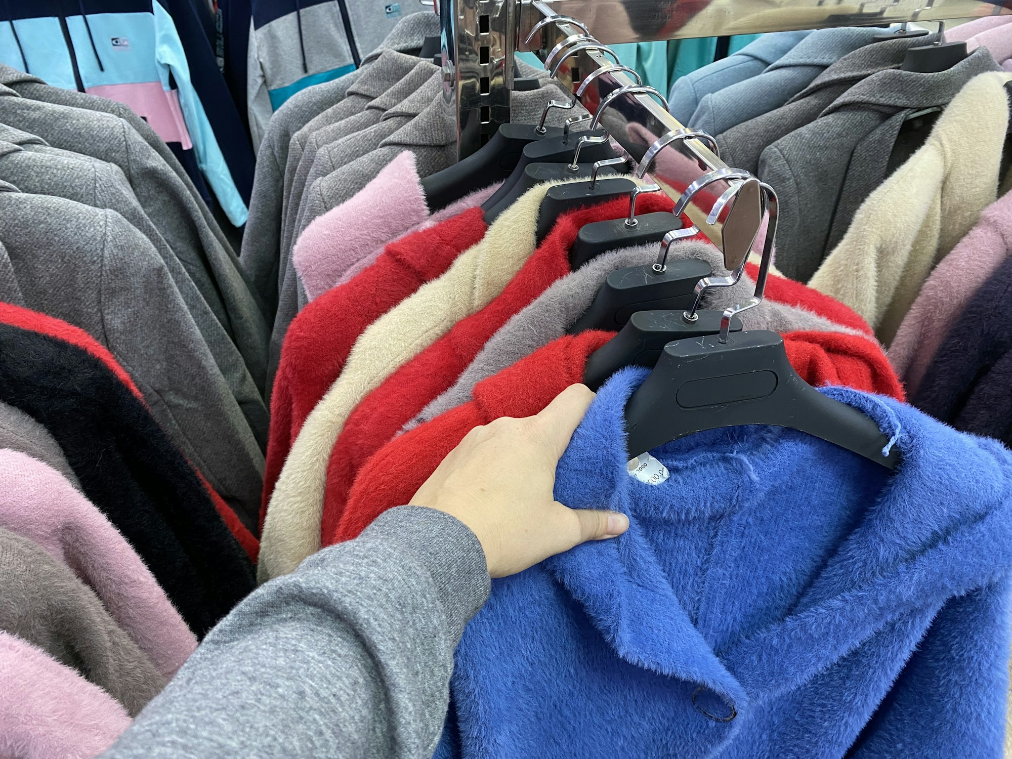 woman chooses a coat (jacket) in the store. a woman's hand takes a blue coat (jacket)